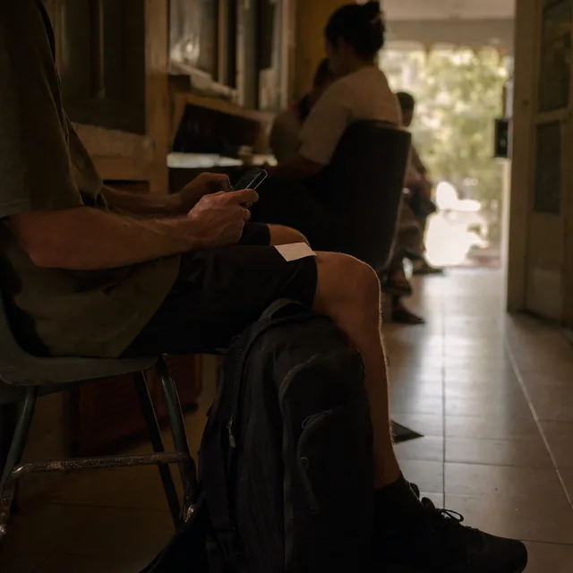 A traveller typing on a phone in a clinic waiting room, a backpack at their feet