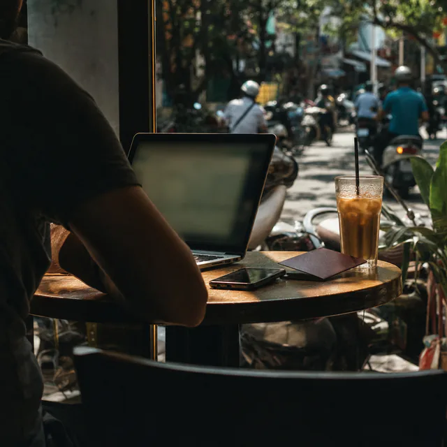 A laptop, a phone and a passport on a cafe table by a sunny window